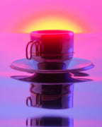 A metal coffee cup with a matching saucer, centered against a vibrant pink and purple background with a glowing yellow-orange light behind it. The cup and saucer are highly reflective, showing strong color reflections and a mirrored reflection below.