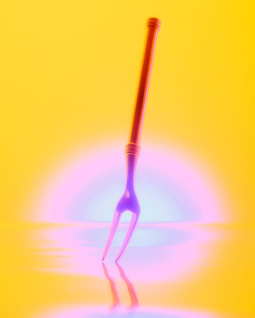 A neon-colored two-pronged fork standing upright on a reflective yellow surface against a glowing yellow background with pink and blue light effects.