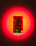 A clear glass jar filled with green olives on the pit, set against a glowing red and orange circular light effect on a dark background.