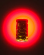 A clear glass jar filled with green olives on the pit, set against a glowing red and orange circular light effect on a dark background.