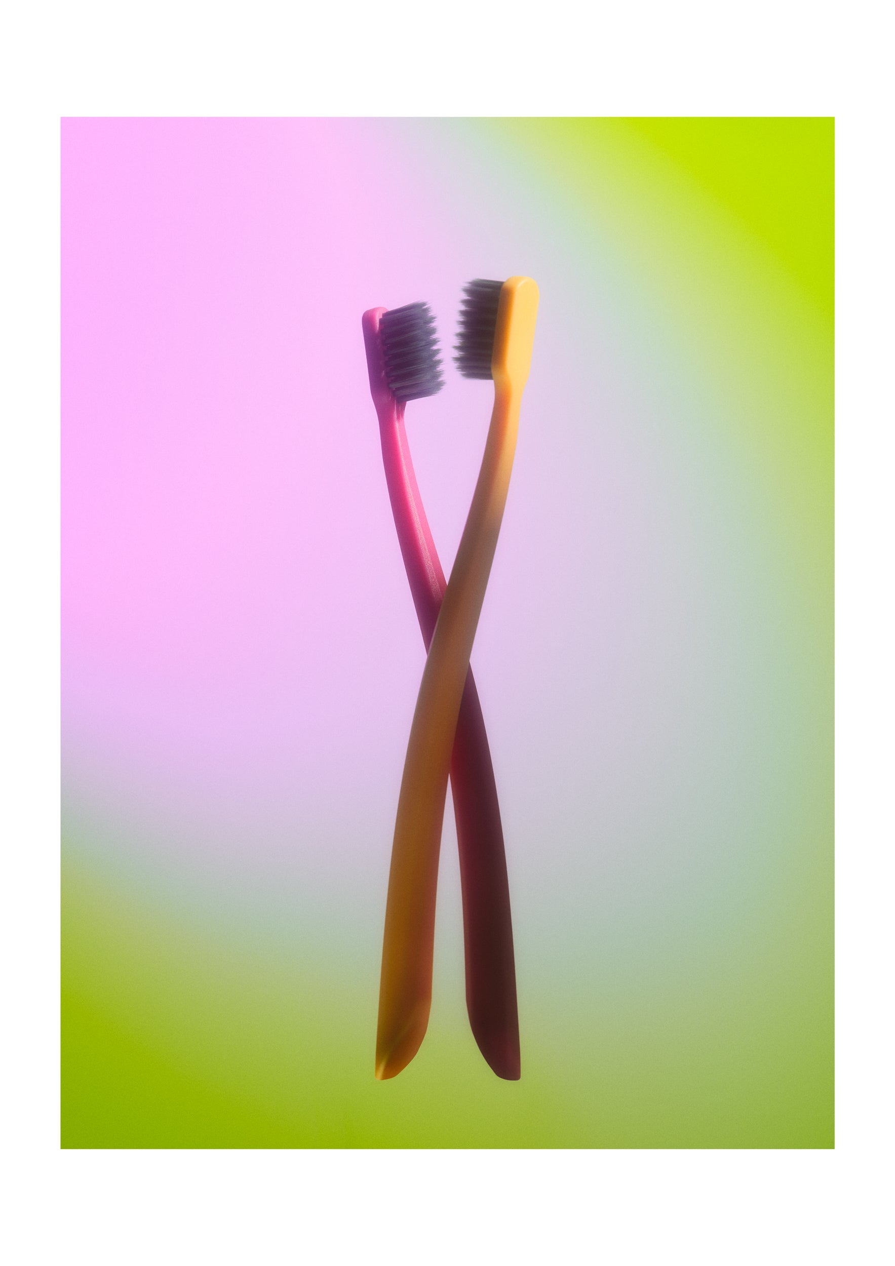Two crossed toothbrushes with pink and orange handles against a soft pink, green, and yellow gradient background.